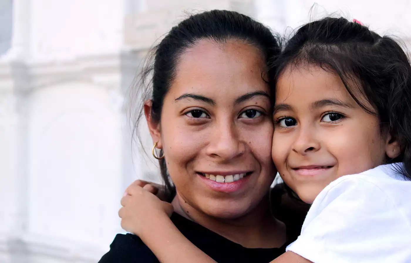 Close-up of a Latina mom holding her daughter. Both smile at the camera