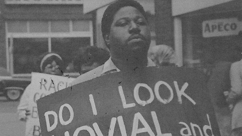 Black man holding a protest sign that says, "Do I look jovial and…" in the 60s Civil Rights movement